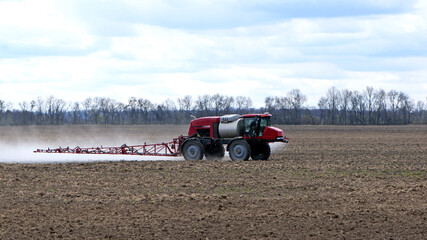 Obraz premium Red tractor with irrigation system watering a field on a cloudy day. agricultural machinery, work in the field. seasonal work. tractor fertilizes the ground