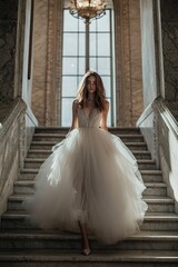 Fototapeta premium Elegant bride descends grand staircase, wearing flowing tulle go