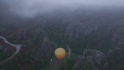 Belogradchik, Bulgaria - 01 December 2024: Aerial view of serene hot air balloon floating over beautiful rocky landscape and tranquil valley surrounded by misty mountains, Belogradchik, Bulgaria.