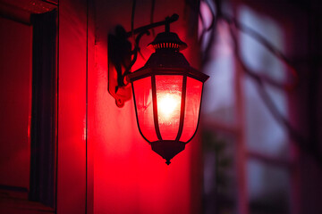 A red outdoor lantern glows brightly at night, casting a warm light on the surrounding wall.