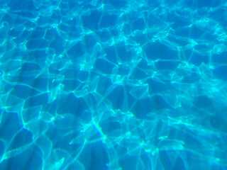 Blue water in the swimming pool with light reflections. Clear Water Caustic Texture, Clear Blue Turquoise Water Surface Shimmering in Sun on Sunny Day, Slow Motion. Blue Green Water in Pool. top view.