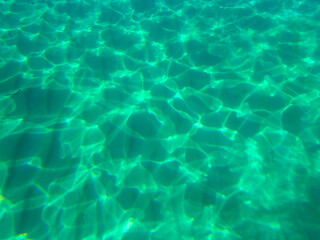 Blue water in the swimming pool with light reflections. Clear Water Caustic Texture, Clear Blue Turquoise Water Surface Shimmering in Sun on Sunny Day, Slow Motion. Blue Green Water in Pool. top view.