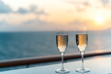 Obraz premium Two glasses of champagne on table with sunset view over ocean, creating romantic and serene atmosphere. Perfect for celebrations or special moments