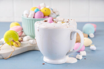 Easter hot chocolate with whipped cream, marshmallow and crushed chocolate mini eggs, on colorful table background, with ingredients, copy space