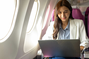 A woman is sitting on a plane with a laptop open in front of her. She is wearing sunglasses and she is working on her laptop  © Kield KD