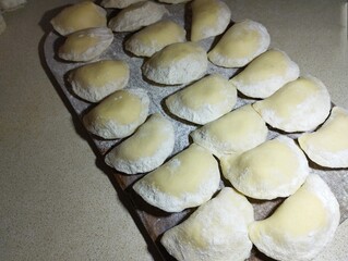 On a wooden board, prepared raw dumplings with potatoes are laid out in three rows. The theme of national Ukrainian cuisine.