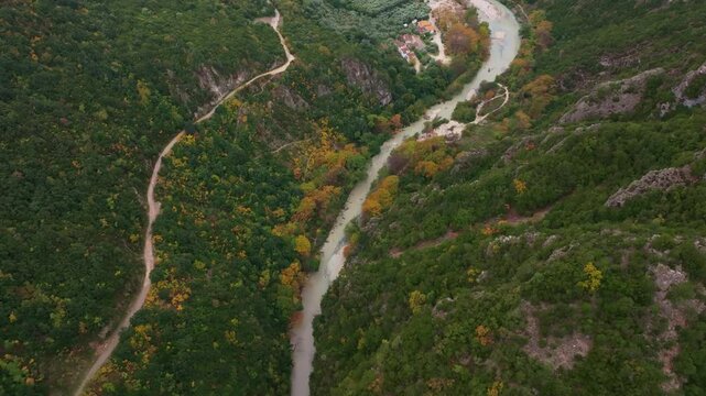 Aerial view of winding river through lush greenery and rugged mountains in Acheron Springs, Epirus, Greece.