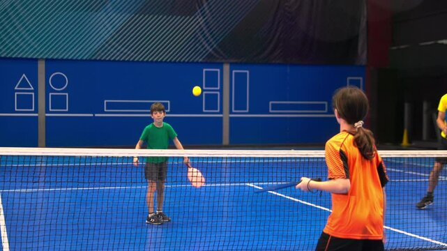 Two adults and two children posing after playing pickleball on a blue, inside court