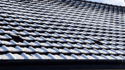 A tiled roof partially covered with fresh snow, illuminated by bright winter sunlight on a cold day