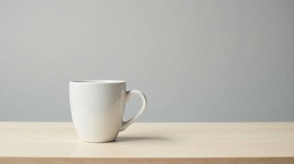 Fototapeta premium A simple white mug sits on a light wood surface against a muted grey background