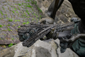 Close-Up of a Bronze Hand Holding a Bundle of Wheat Stalks on Cobblestone Background