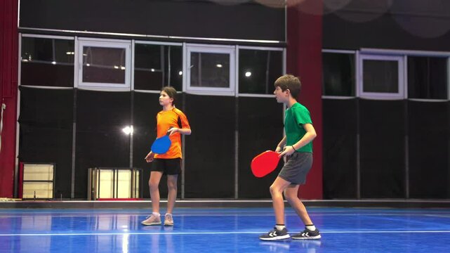 A man teaching his son to play pickleball on a blue, inside court