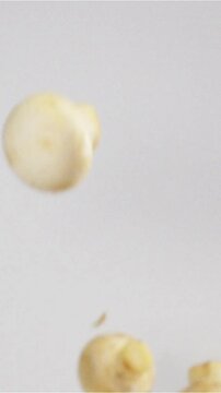 Champignons in the Kitchen. Button mushrooms thrown up on a white bg. Pieces hang in the air. Filmed at a speed of 500fps Vertical Shot.