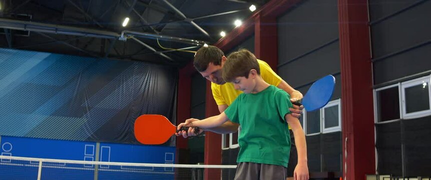 A boy and a girl playing pickleball on a blue, inside court