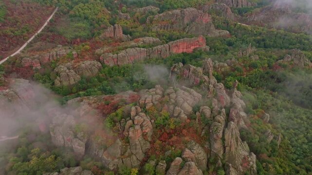 Aerial view of vibrant autumn rocks and serene forest under clouds, Belogradchik, Bulgaria.