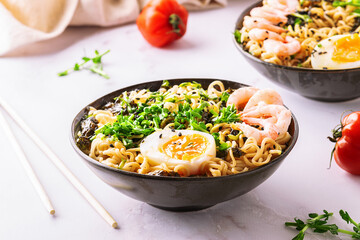 Ramen noodles with egg, shrimps, greens, seasame, seaweed and spices on white marble table close up. Traditional Asian soup.
