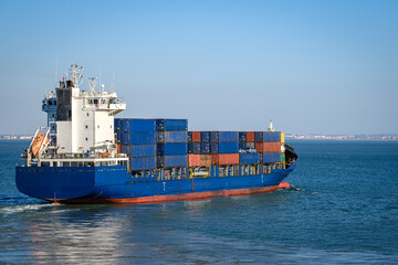 Blue container ship loaded with cargo containers sailing on sunny day