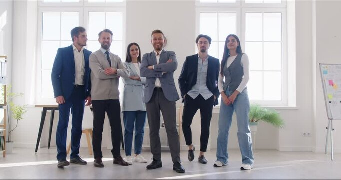Slow motion video of confident business people looking cheerful at camera with crossed arms and smiling indoors. Company employees group standing in office on a meeting. Teamwork concept. 4k video.