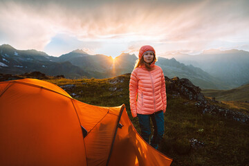 Woman trekking with tent camping gear in mountains hiking travel adventure outdoor, healthy lifestyle summer active vacations trip - girl in warm down jacket enjoying sunset landscape