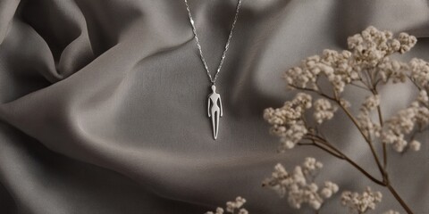 Modern silver necklace featuring human figure pendants, elegantly displayed on textured gray fabric, complemented by whimsical child like sketches for a playful touch.