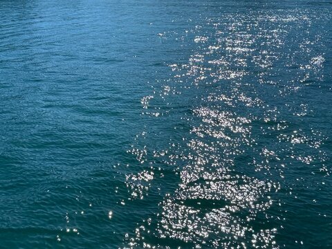 Blue sea glittering sun reflections on calm water.