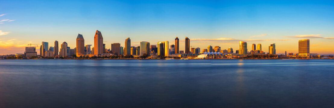 Panoramic view of San Diego's skyline at sunset, captured from Coronado Island with a long exposure, highlighting calm waters and city lights.