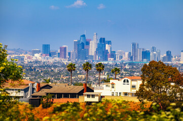Naklejka premium Los Angeles skyline on a clear day, captured from Kenneth State Park, with residential homes, palm trees, and greenery in the foreground.