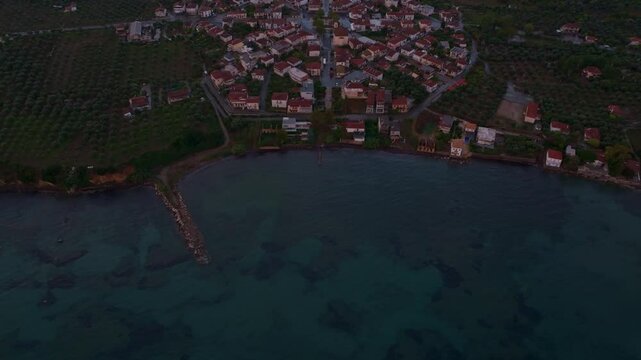 Aerial view of a beautiful coastal village with olive groves and rooftops at sunset over the Ionian Sea, Nea Koroni, Greece.