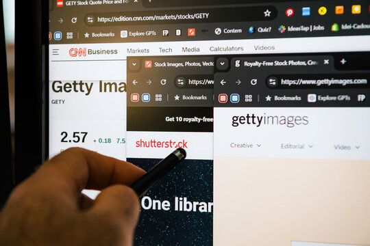 Paris, France - Jan 7, 2025: Multiple browser tabs showcasing Getty Images and Shutterstock platforms, with a hand pointing at the screen. Stock prices and site details are visible.