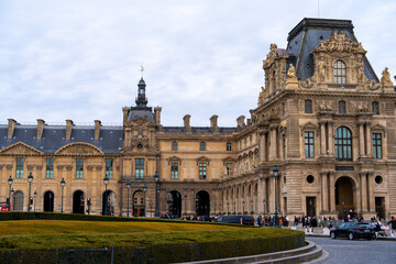 Fototapeta premium Visitors explore the historic architecture and courtyard of the Louvre Museum in Paris during a cloudy afternoon