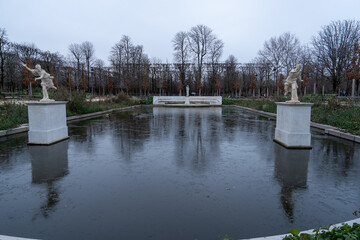 Serene pond with statues and bare trees in a public park during a cloudy day in early winter