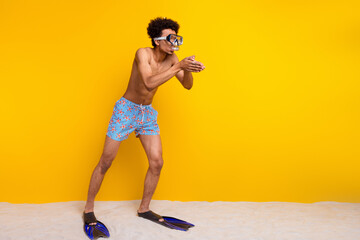 Young african american man wearing swimwear and snorkel gear stands in sand against bright yellow...