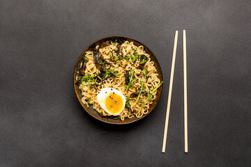 Ramen noodles with egg, greens, seasame, seaweed and spices on black stone table close up....