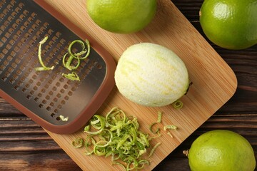 Lime zest, grater and fresh fruits on wooden table, flat lay