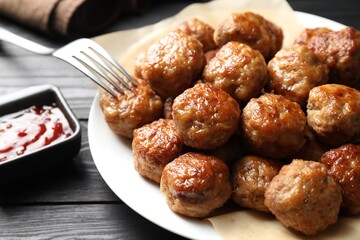 Many delicious meatballs served with ketchup on dark wooden table, closeup