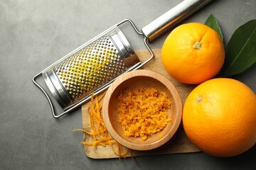 Orange zest, grater and fresh fruits on gray textured table, flat lay
