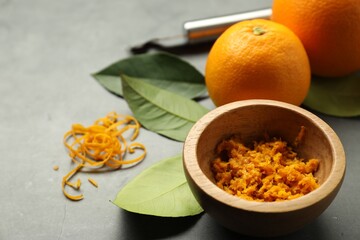 Orange zest in bowl and fresh fruits on gray textured table, closeup. Space for text