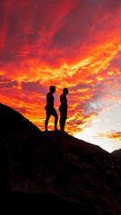 Two men stand a top of a rock in the blazing sunset created by clouds in the sky. Western Cape, South Africa.