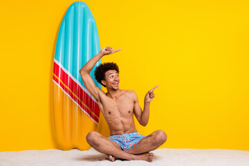 Young man enjoying summer fun sitting on the beach with a vibrant surfboard on a bright yellow...
