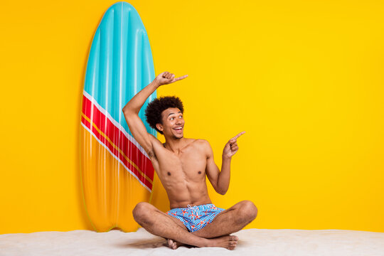 Young man enjoying summer fun sitting on the beach with a vibrant surfboard on a bright yellow background.