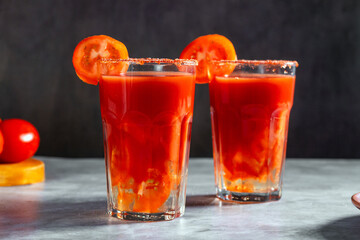 Two Bloody Mary cocktails in glass served with tomato slice and salt on dark background. Red cocktail. Alternative taste. Dirty dump drink