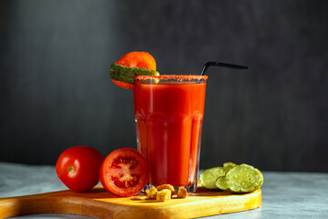 Vegetable shaken cocktail in glass on dark grey background. Red tomato cocktail. Served with tomatoes and pickles. Vegan menu.
