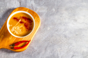 Pumpkin soup with chili pepper and cream on wooden tray on light table. Flat lay with copy space. Cream soup. Concept of tasty healthy food.
