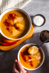 Woman tasting pumkin soup with spoon. Eating cream soup. High angle. Served table with soup bowl, pepper, chili, salt.