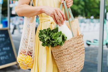 Woman holding bags with fresh organic food on storefront background of zero waste shop.