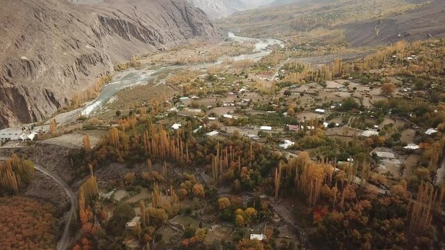 Aerial view of the beautiful Gilgit River winding through a picturesque valley surrounded by majestic mountains and a tranquil village, Gupis, Pakistan.