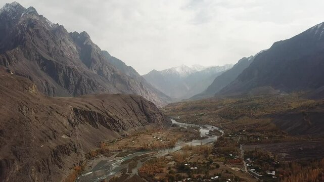 Aerial view of the majestic Gilgit River flowing through a serene valley surrounded by rugged mountains, Gupis, Pakistan.