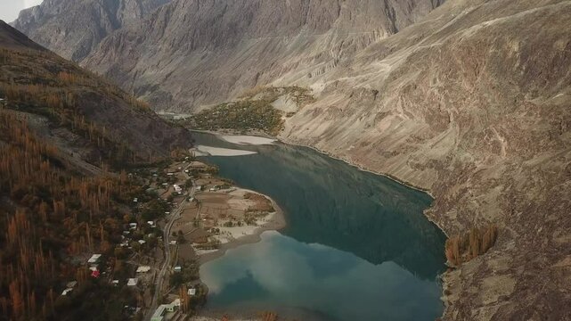 Aerial view of the majestic Gilgit River winding through a serene valley surrounded by rugged mountains and a picturesque village, Gupis, Pakistan.