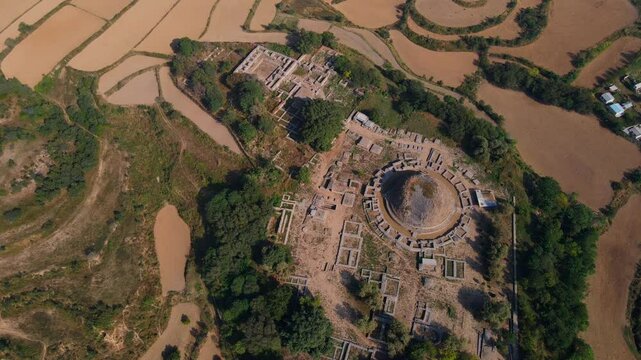 Aerial view of Dharmarajika Stupa ruins surrounded by lush greenery and fields, Taxila, Pakistan.