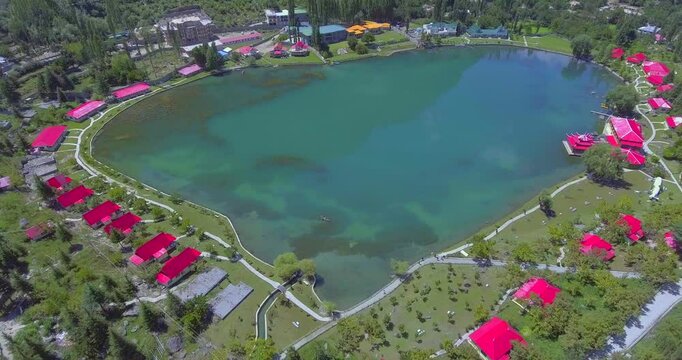Aerial view of serene Lower Kachura Lake with vibrant red roofs of Shangrila Resort surrounded by lush greenery and mountainous landscape, Skardu, Pakistan.